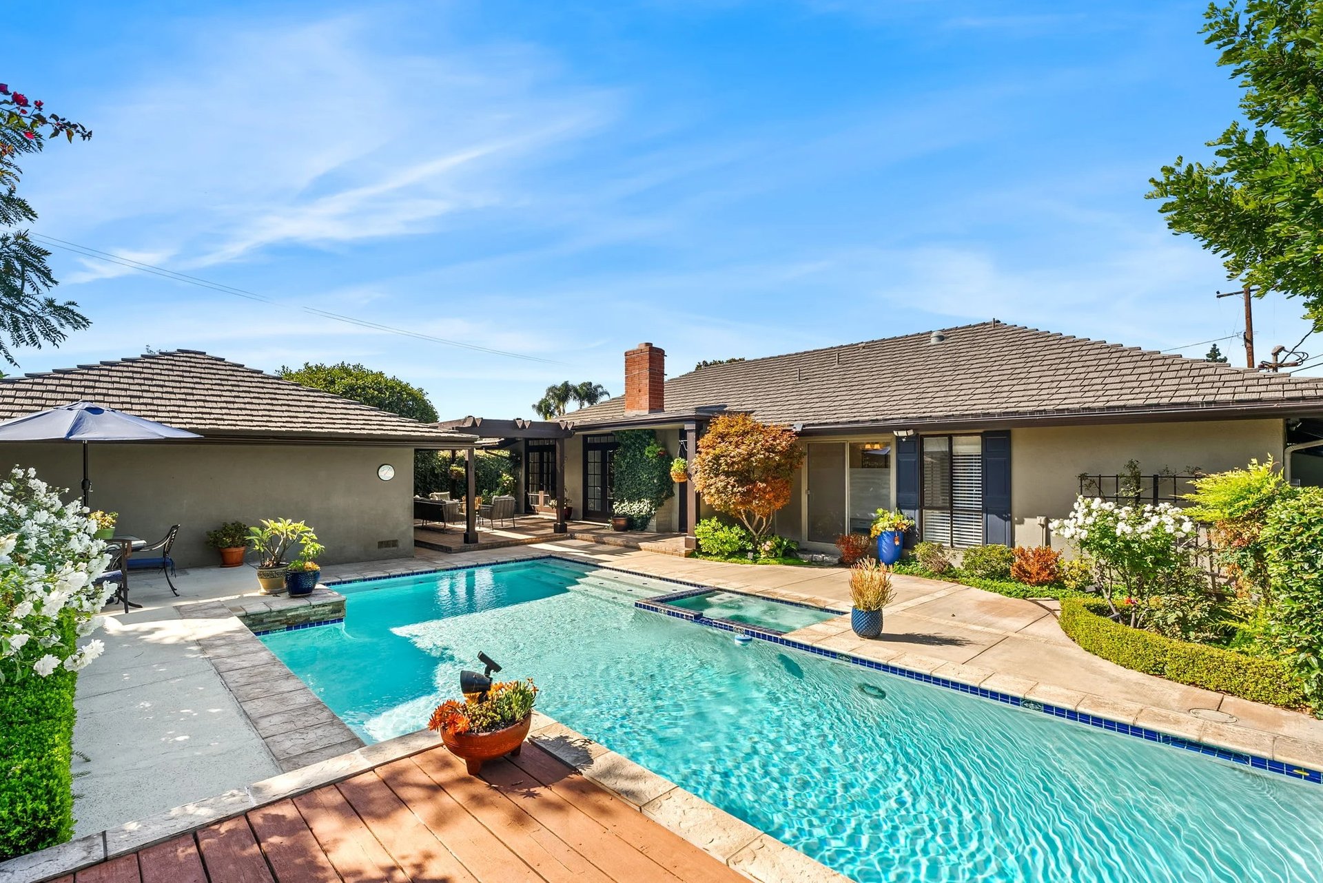 Home surrounding a turquoise swimming pool, with a landscaped patio, outdoor seating, and potted plants.