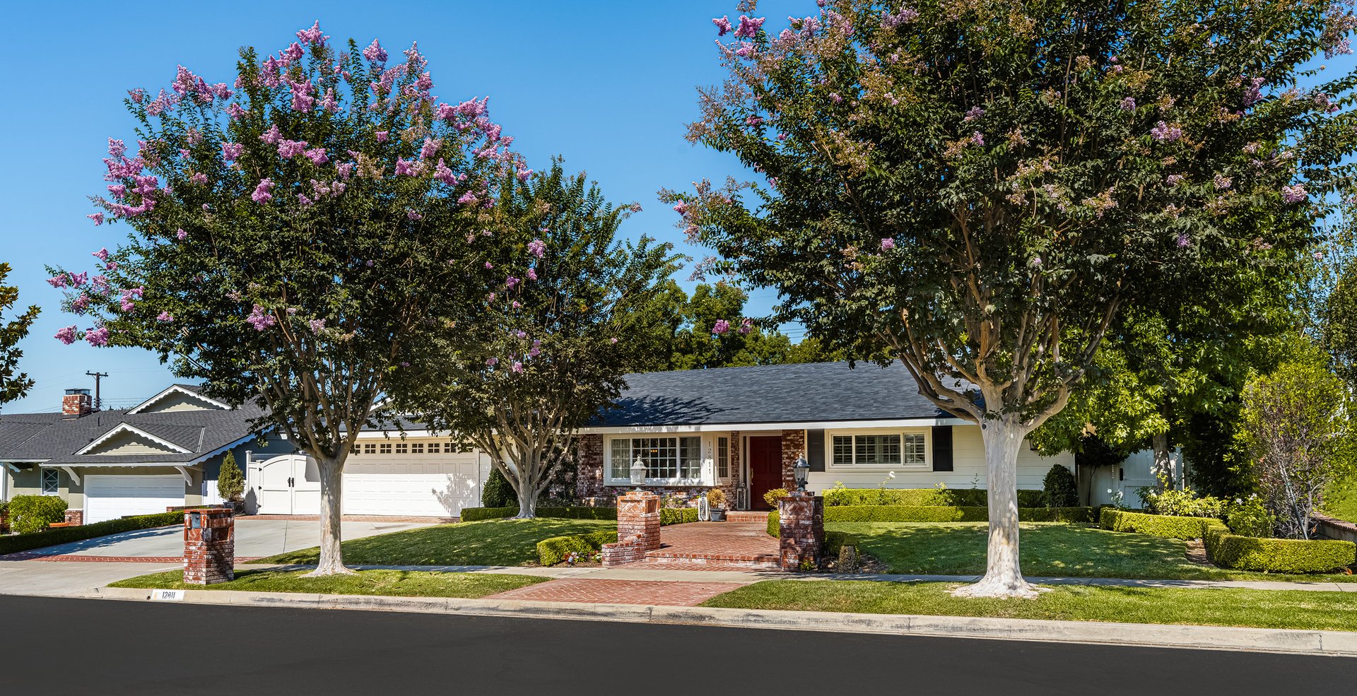 Single-story house with an attached garage, brick entry path, and flowering trees.