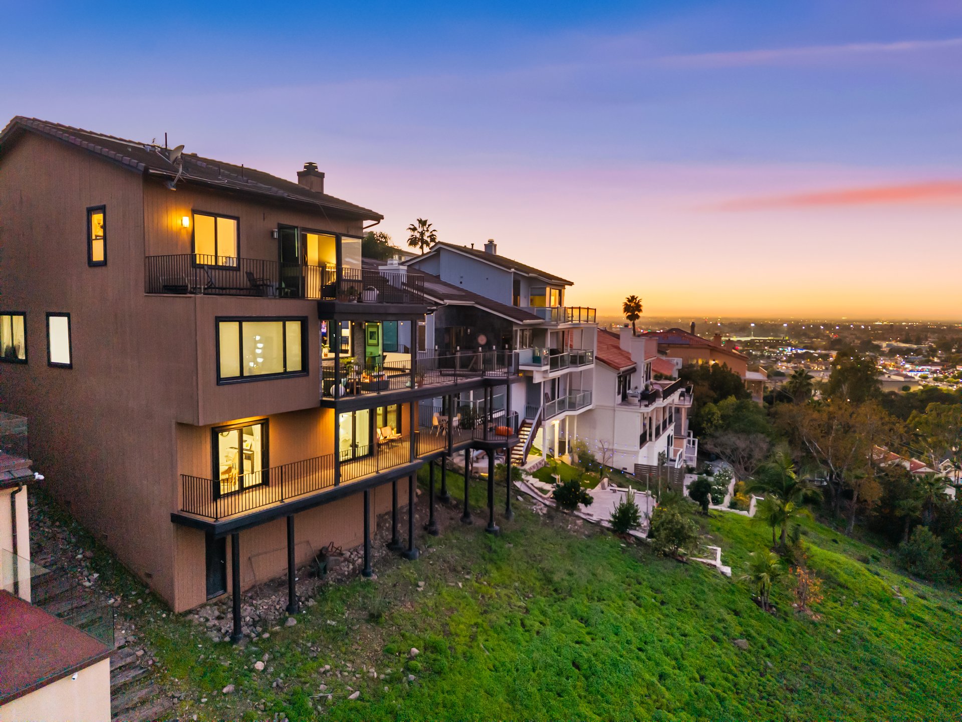 Hillside home with illuminated balconies overlooking the city at dusk.