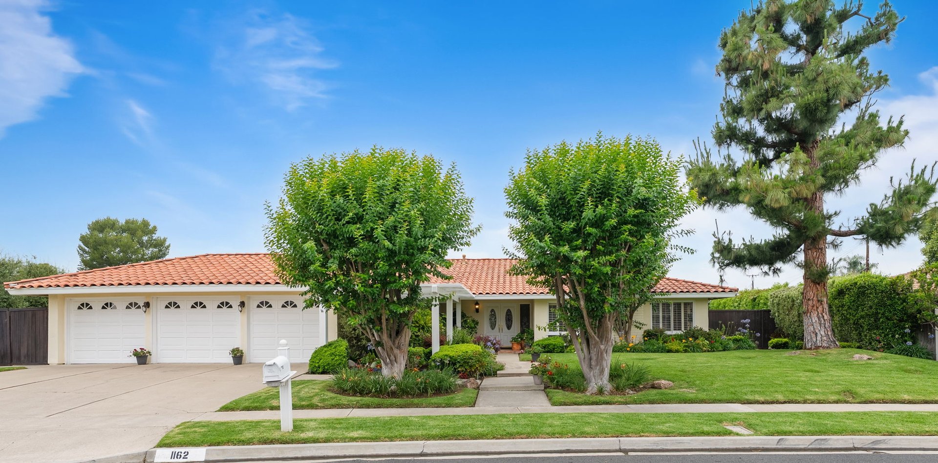 Single-story white home with a terracotta tile roof, three-car garage, and landscaped front yard.