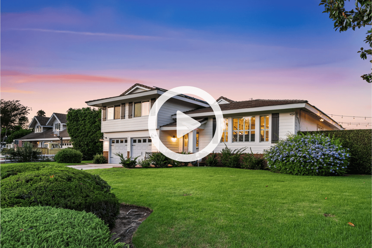 Two-story white home with a broad lawn and flowering shrubs at dusk.