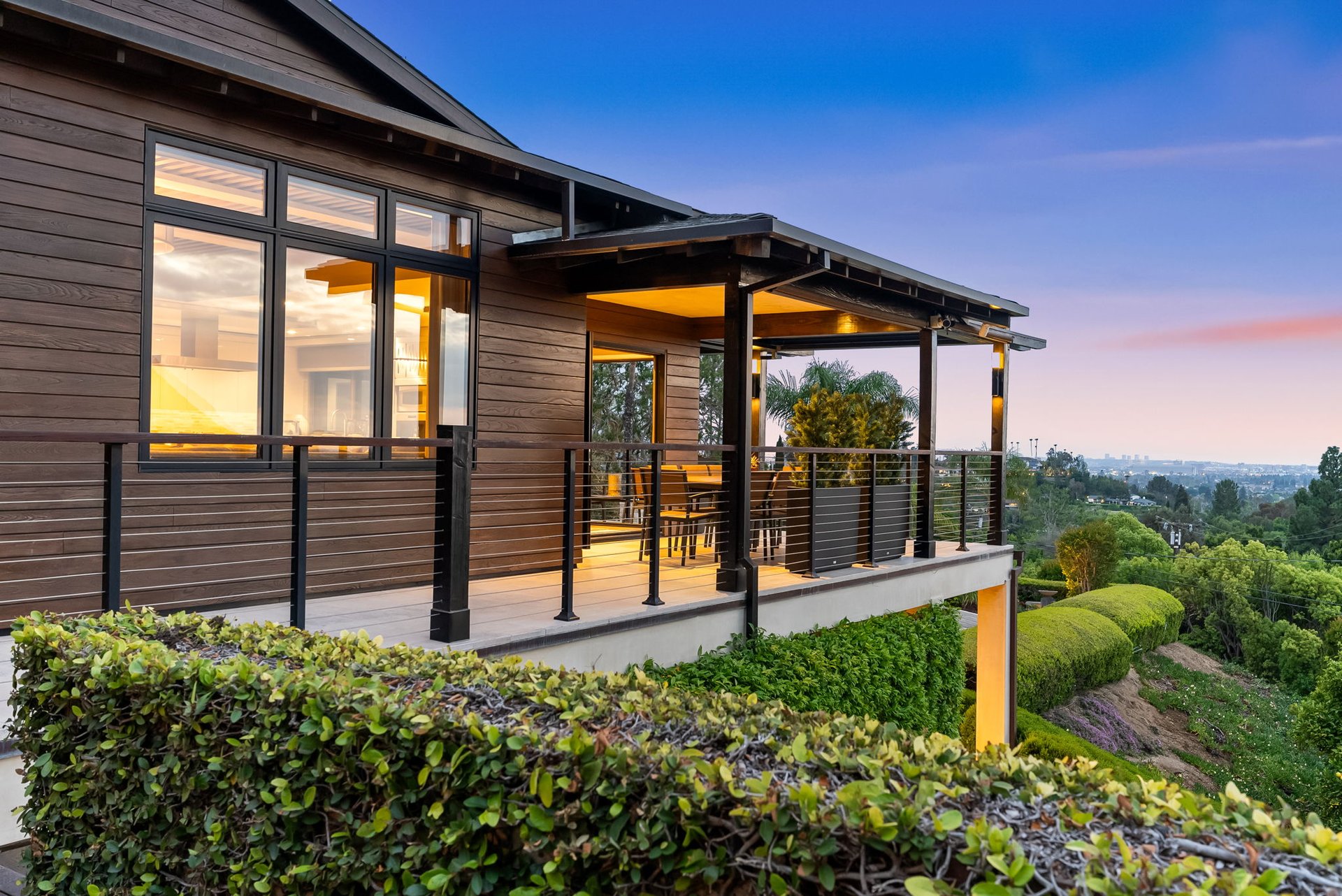 Modern hillside home with an illuminated covered balcony overlooking the city at dusk