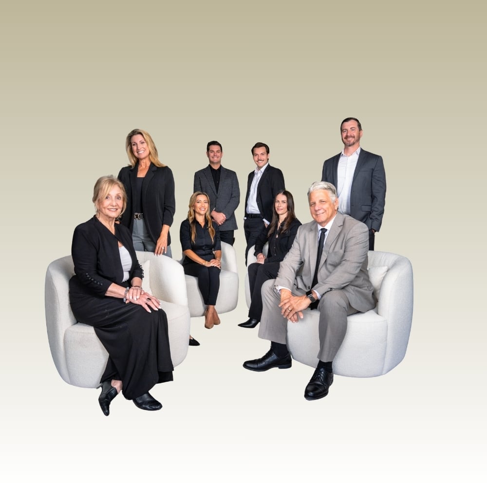Eight real estate agents pose together, seated and standing around two white armchairs.