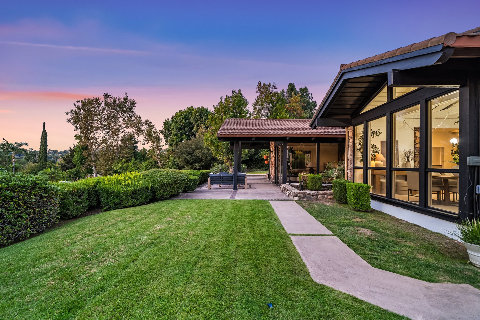 Modern home with a covered patio and curved walkway across a landscaped lawn at dusk.