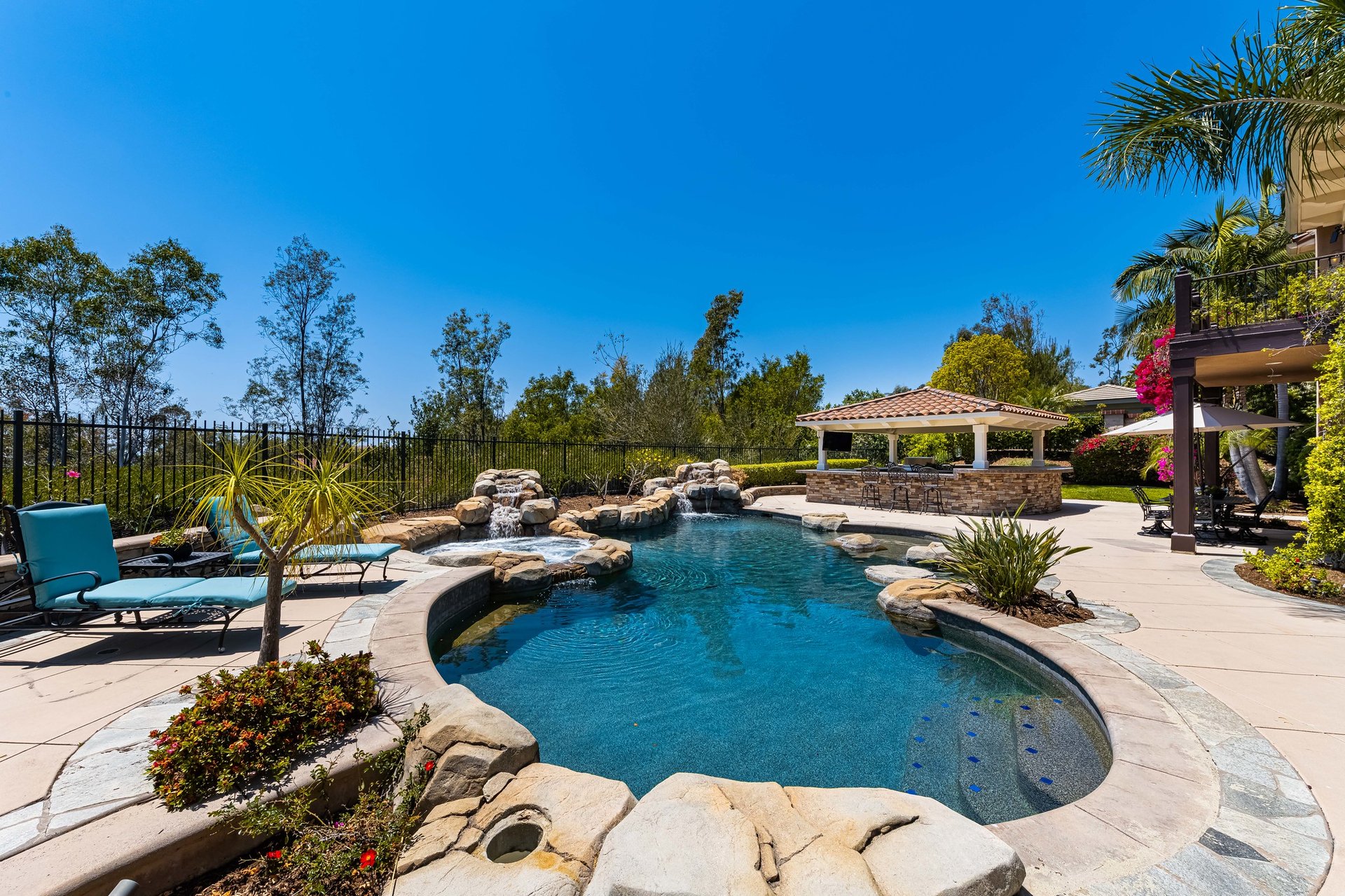 Tustin Ranch pool with a rock waterfall, turquoise lounge chairs, and a shaded pavilion.