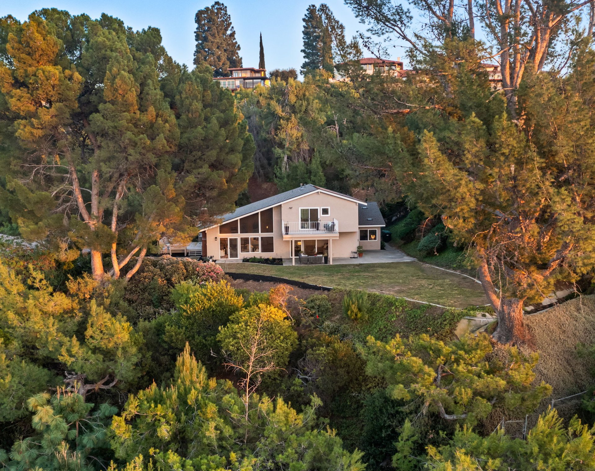 Two-story home nestled among mature trees, with a balcony and landscaped grounds.