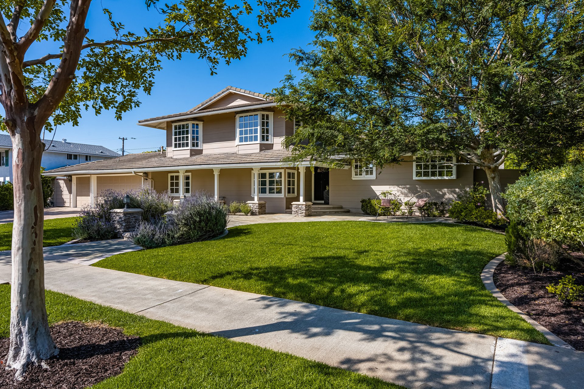 Two-story home with a broad front lawn, mature trees, and a curved concrete walkway.