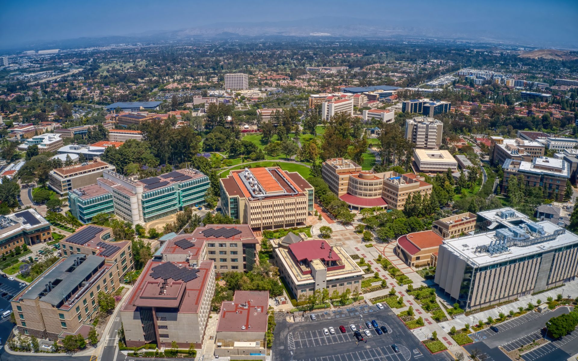Aerial view of a landscaped business district with office buildings, greenery, and distant hills.