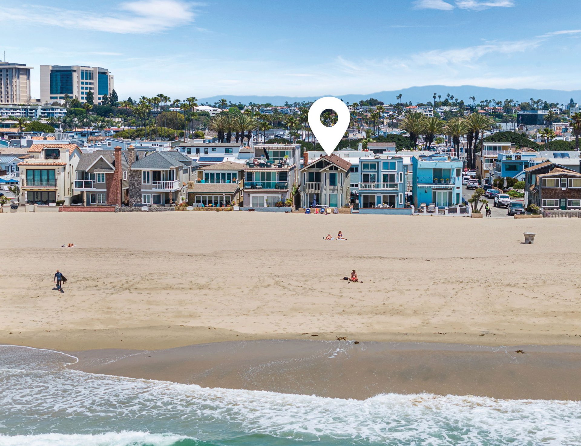 Beachfront homes behind a sandy beach, with a white location pin over one house.