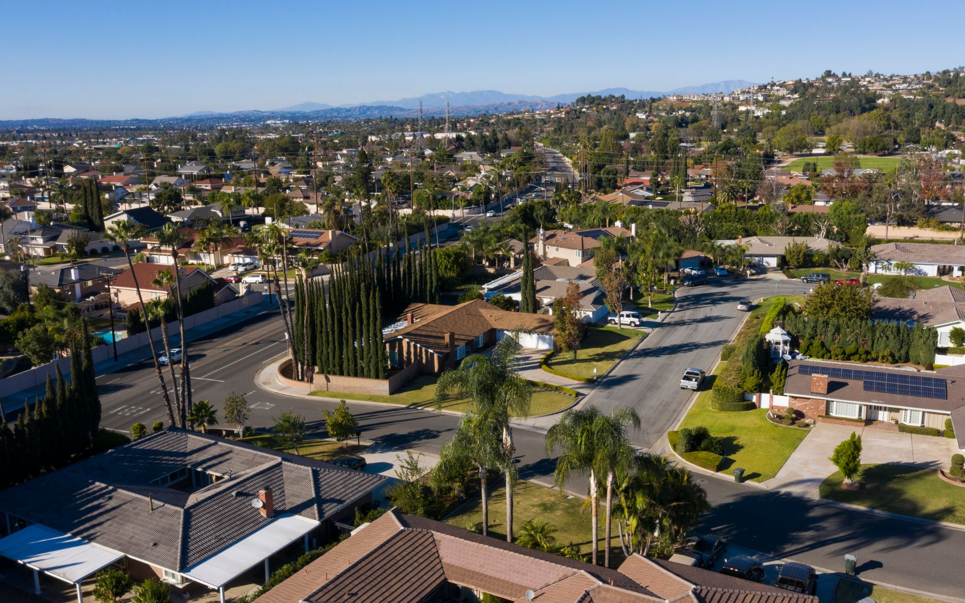 Aerial view of a residential neighborhood with tree-lined streets and hills in the distance.