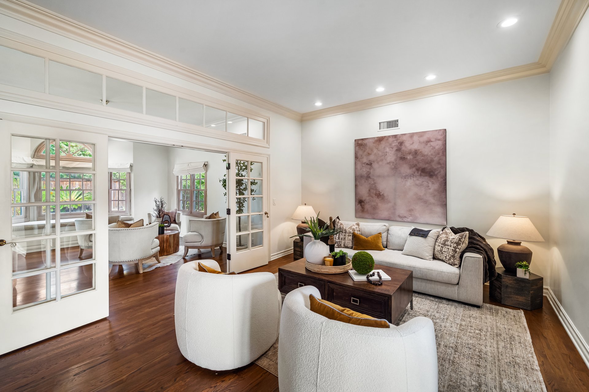 Living room with French doors, a pale sectional, white armchairs, and dark wood floors.