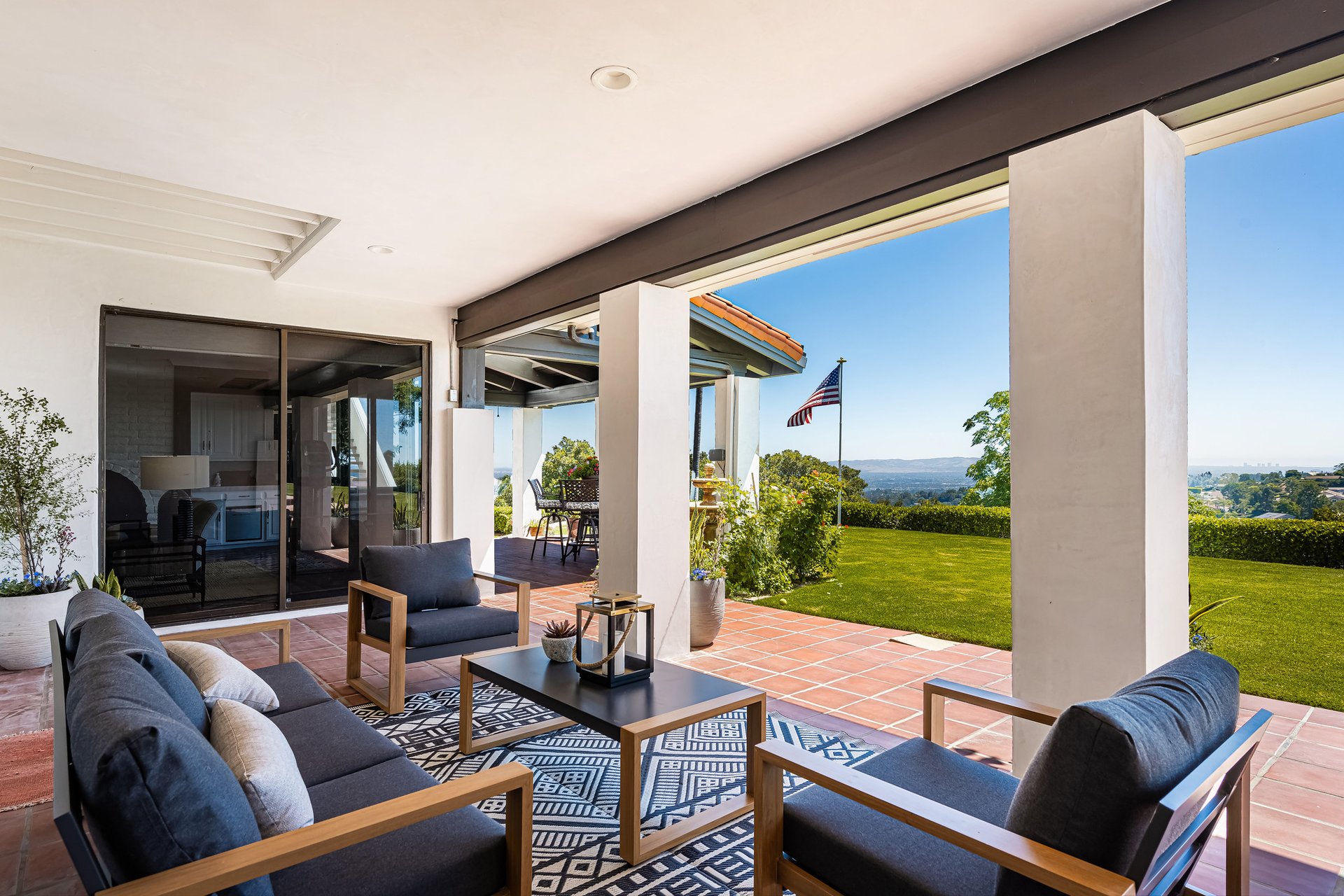 Covered patio with tiled floor and lounge seating overlooking a manicured lawn.