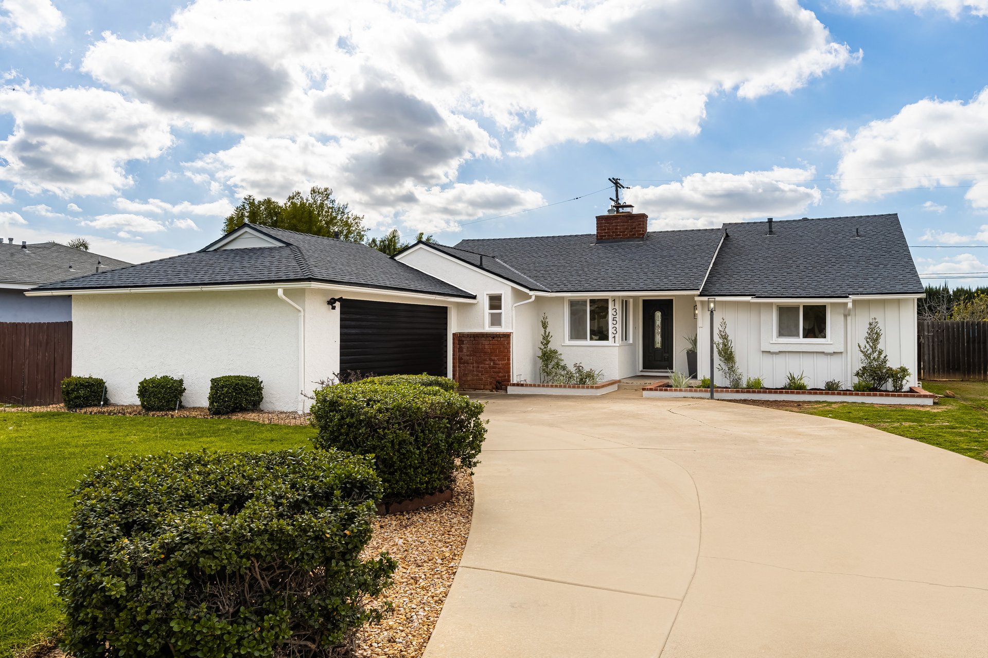 White single-story house with an attached garage, curved driveway, and landscaped front yard.