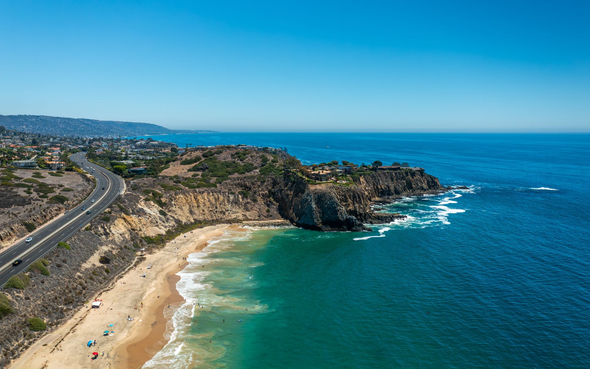 Aerial view of a beach and rugged Pacific coastline beside a winding coastal highway.