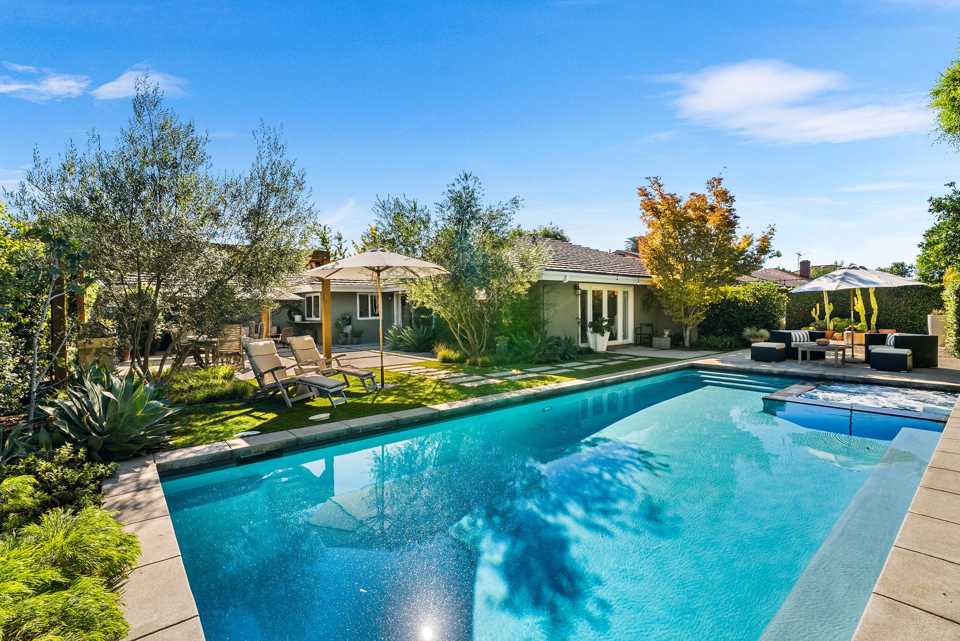 Backyard pool beside a single-story home, with landscaped gardens and shaded patio seating.