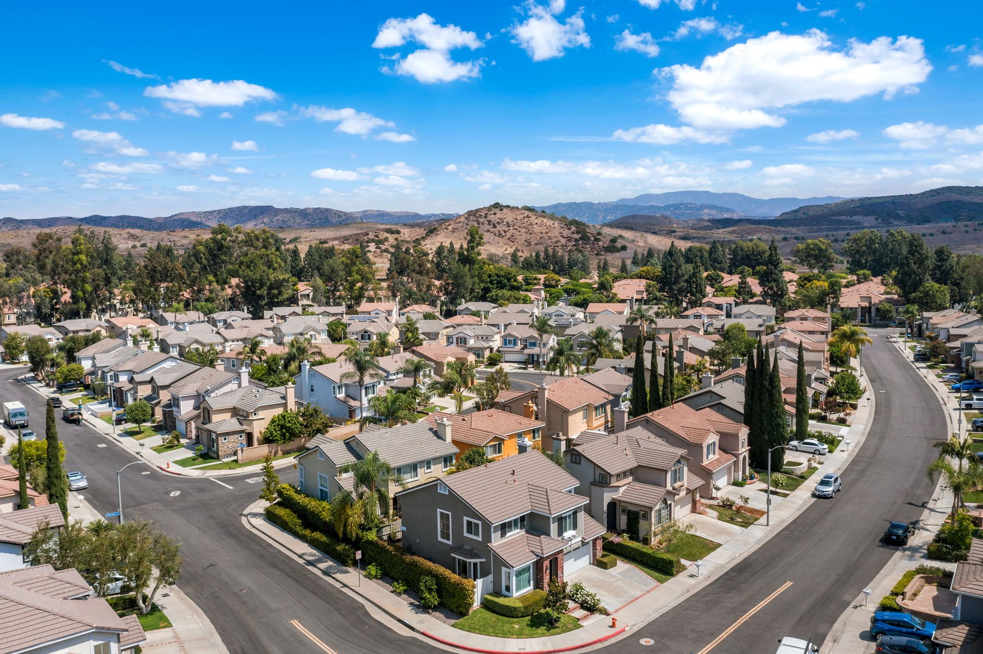Aerial view of a residential neighborhood with curved streets, tree-lined homes, and dry hills beyond.