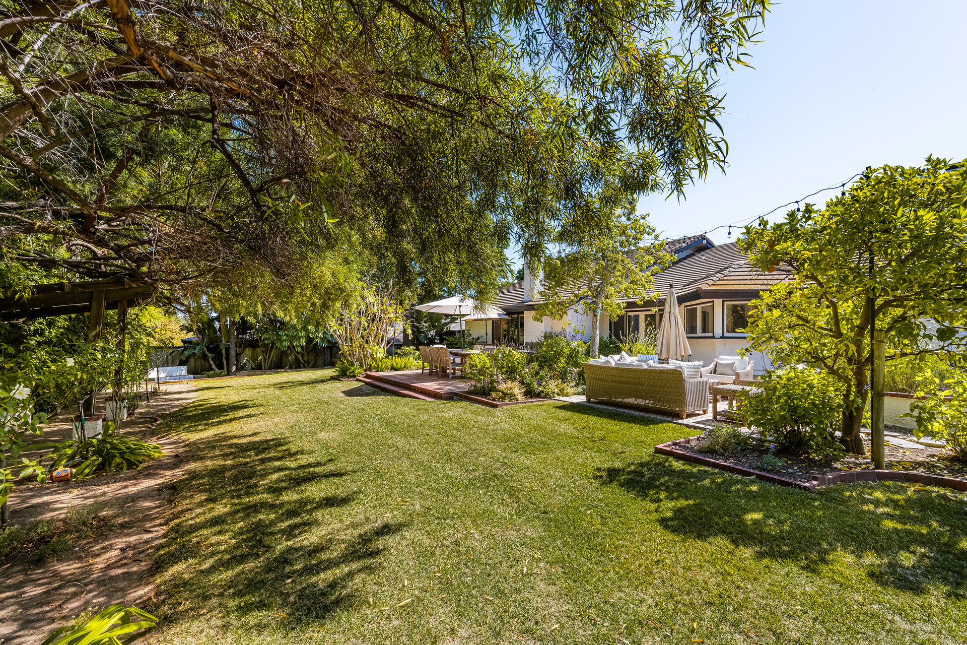 Backyard with a broad lawn, mature trees, and a furnished patio beside the house.