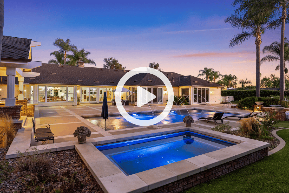 Modern home with illuminated pool and spa beside a broad paved patio at dusk.