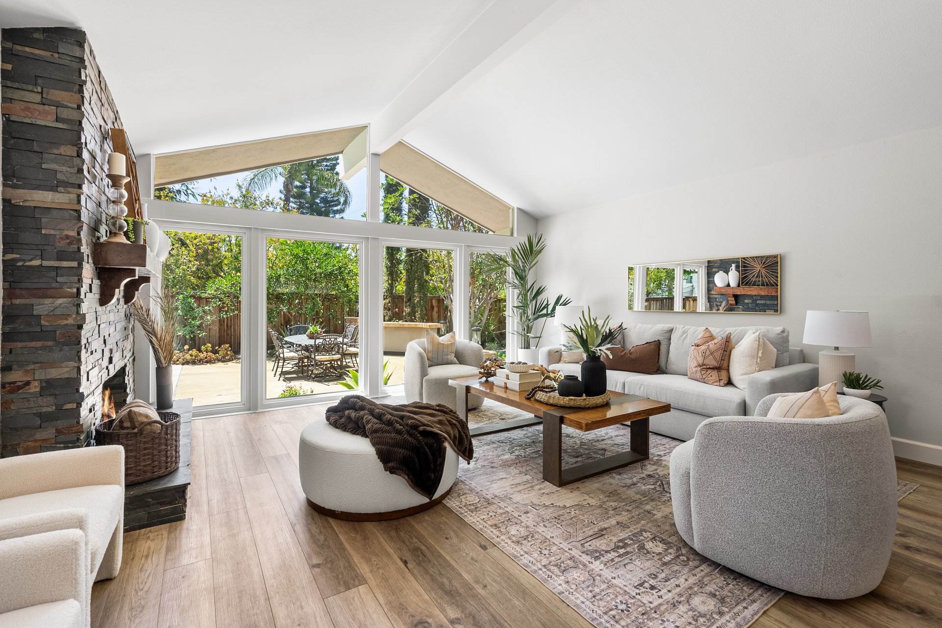 Staged living room with stone fireplace, vaulted ceiling, and glass doors to garden patio.
