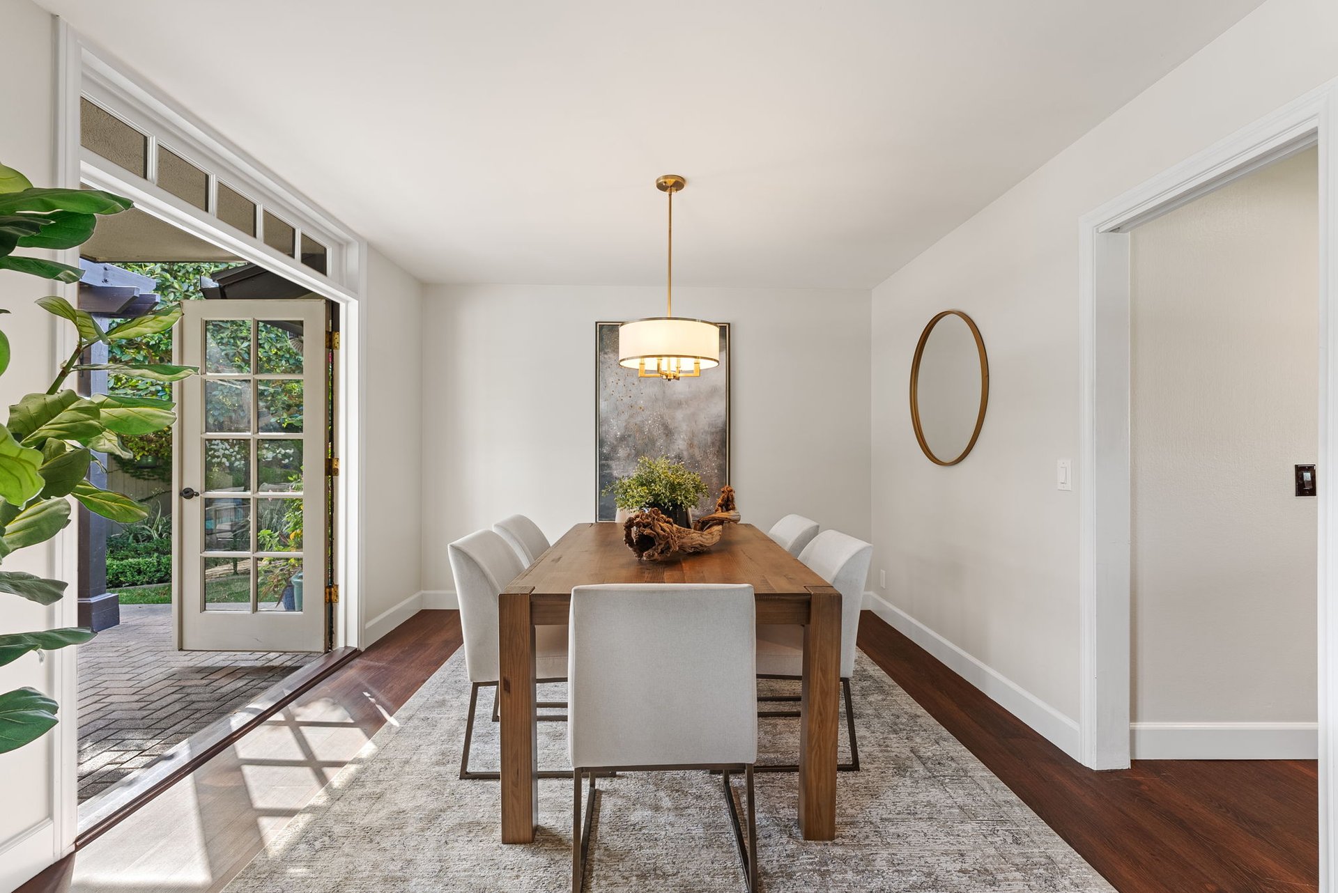 Dining room with a wood table, white chairs, and open French doors to a garden patio.