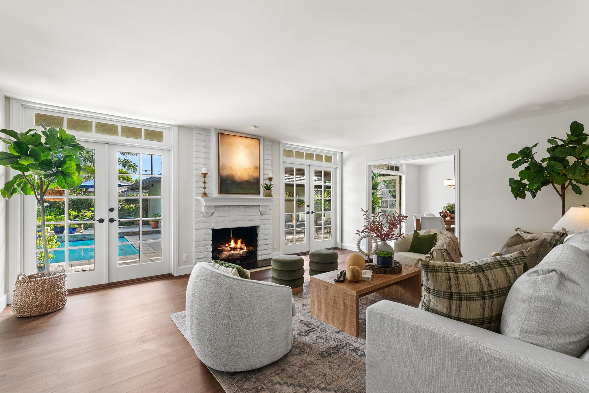 Living room with a lit white-brick fireplace and French doors overlooking a swimming pool.