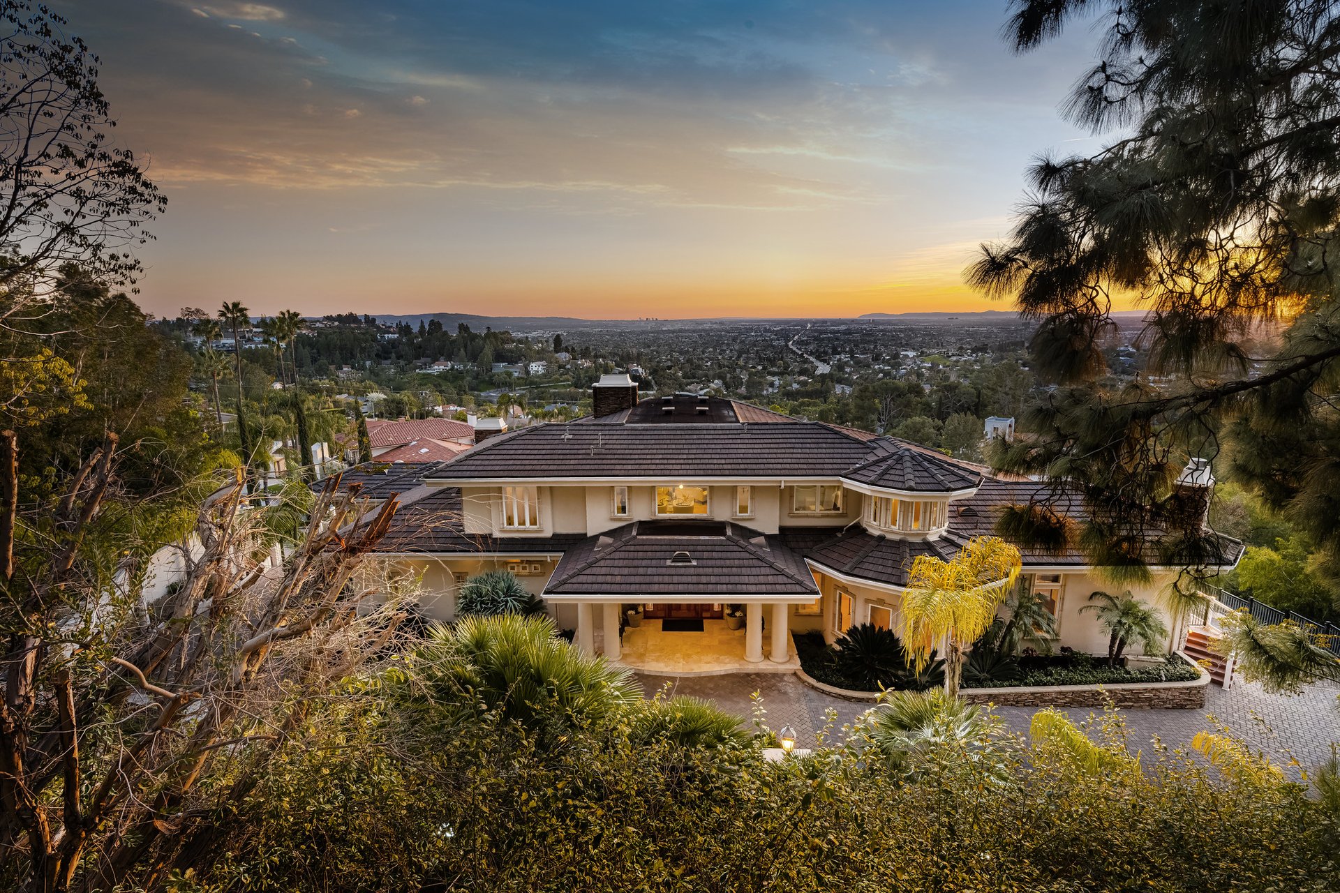 Luxury home with landscaped grounds and a wide city view at sunset.
