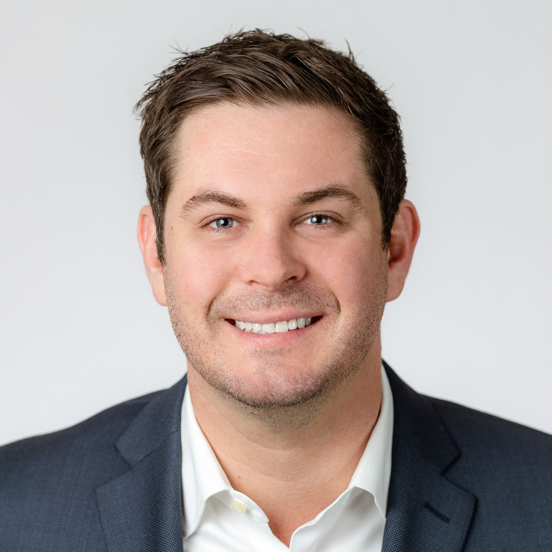 Greg Hendrickson smiling in a dark suit jacket and white shirt.