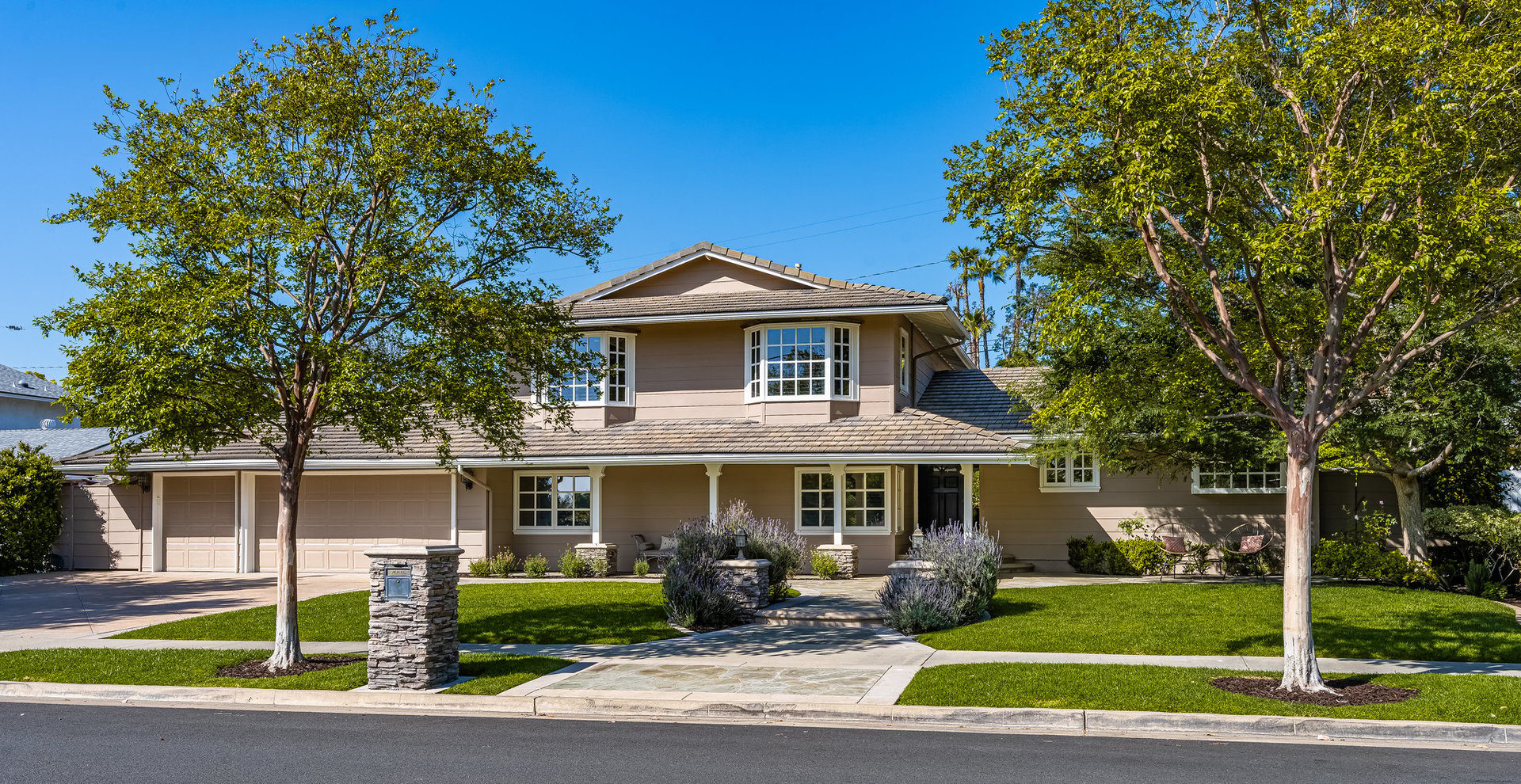 Two-story home with an attached garage, manicured lawn, mature trees, and stone mailbox.