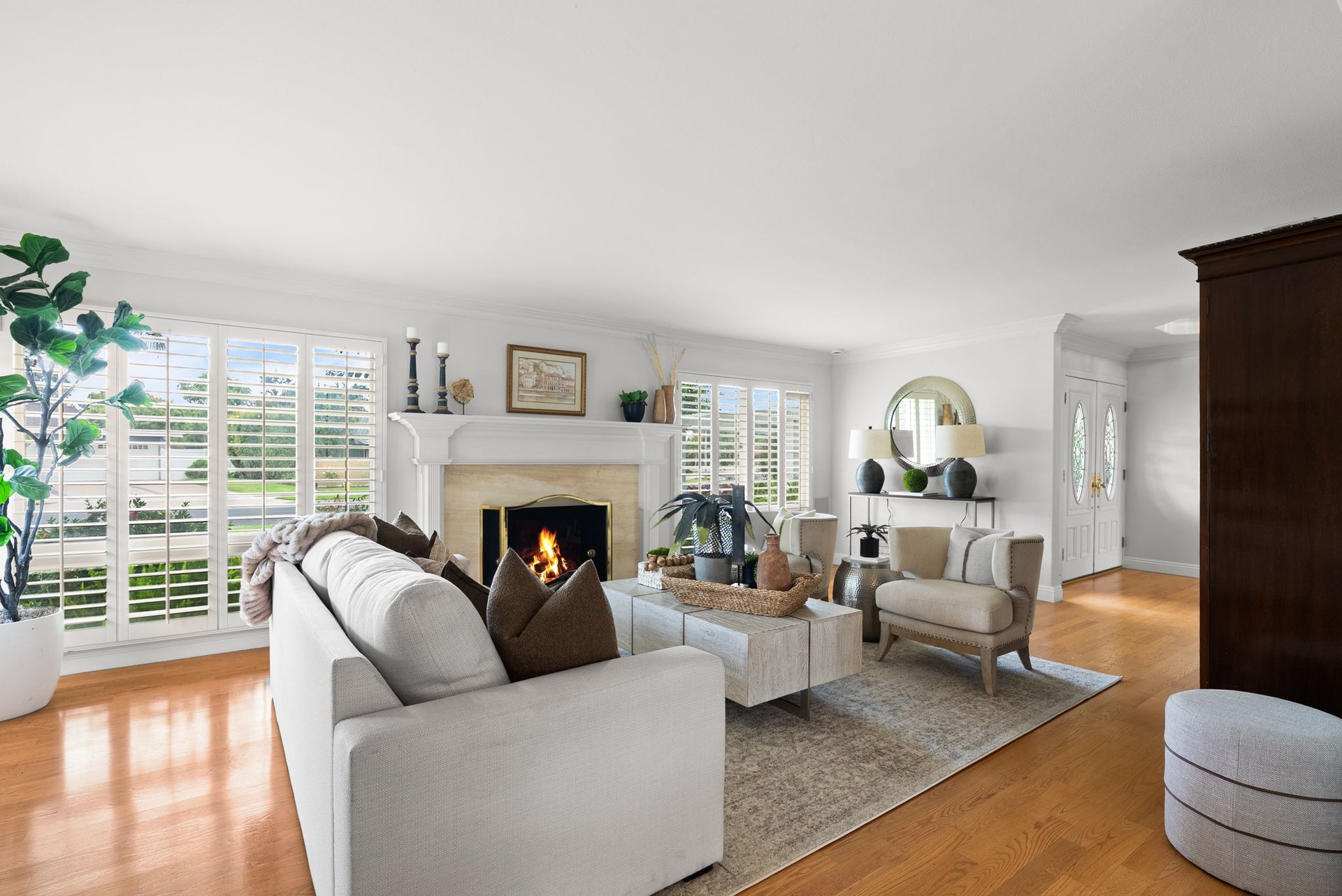 Living room with plantation shutters, a lit fireplace, neutral seating, and hardwood floors.