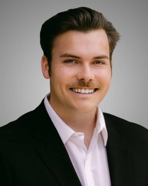 Evan Fredericks smiling in a black suit jacket and white shirt.