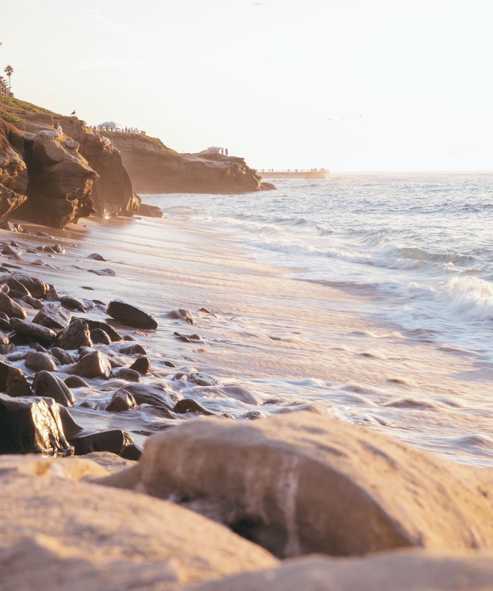Rocky shoreline and coastal cliffs beside the ocean in warm evening light.