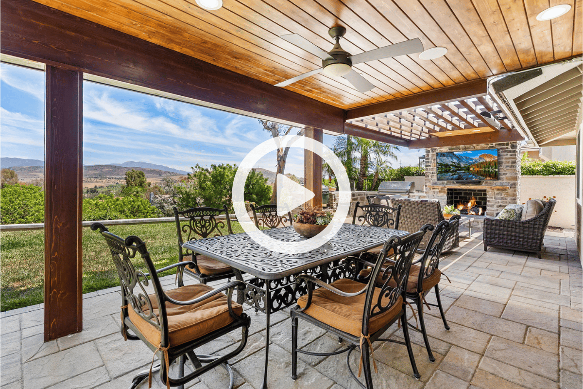 Covered patio with a wood ceiling, stone fireplace, outdoor dining set, and distant hill views.
