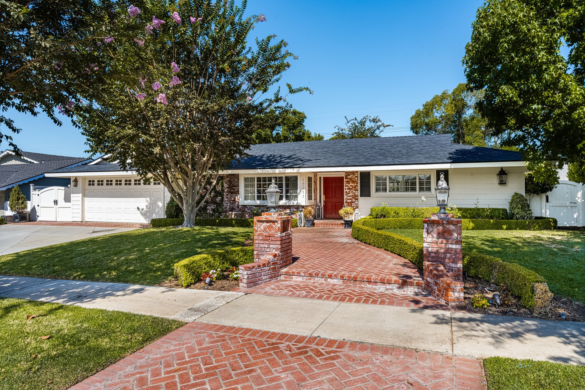 Single-story home with a red front door, two-car garage, and brick walkway through landscaped grounds.