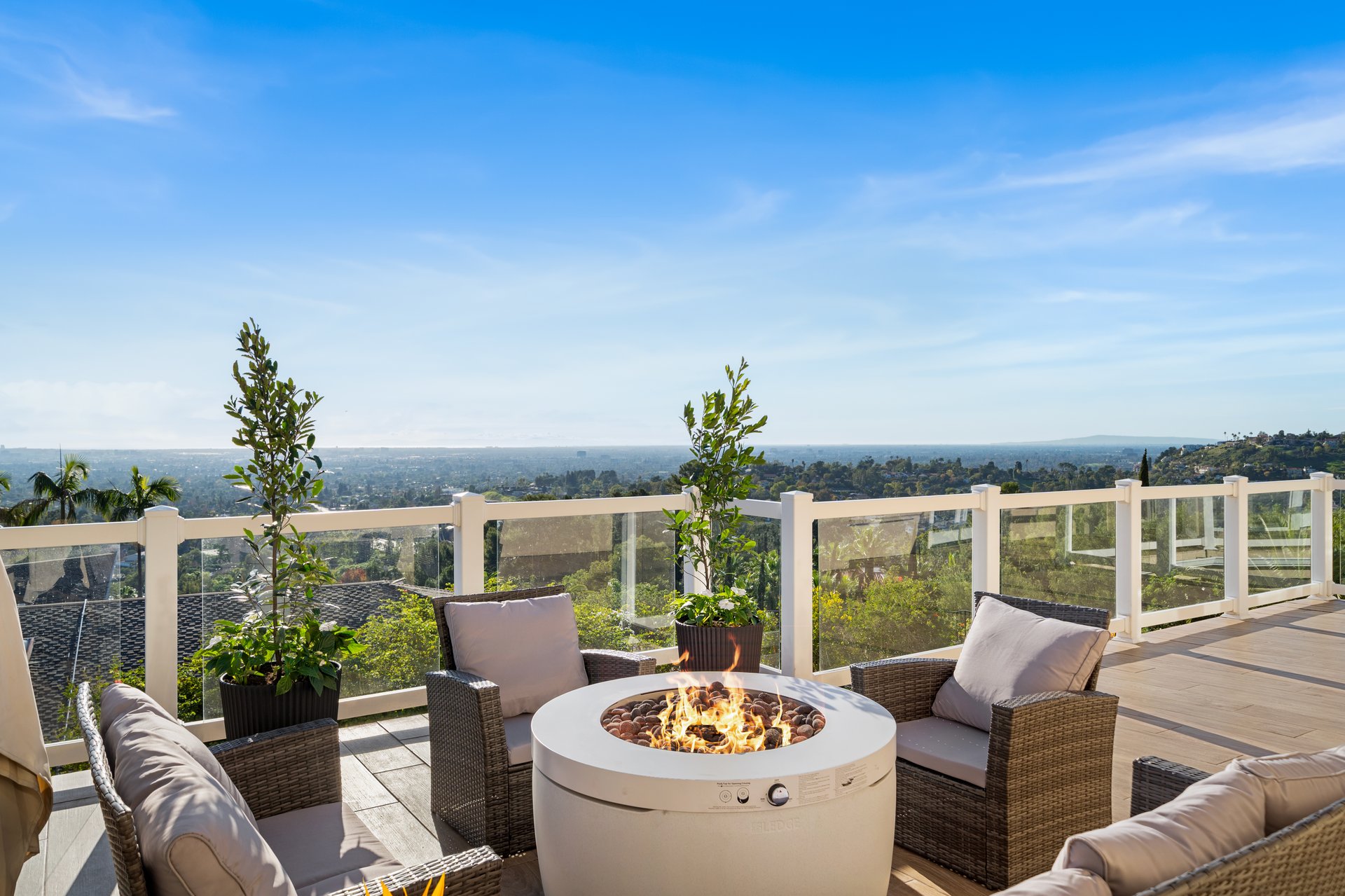 Outdoor terrace with a round fire pit and wicker seating overlooking the city.